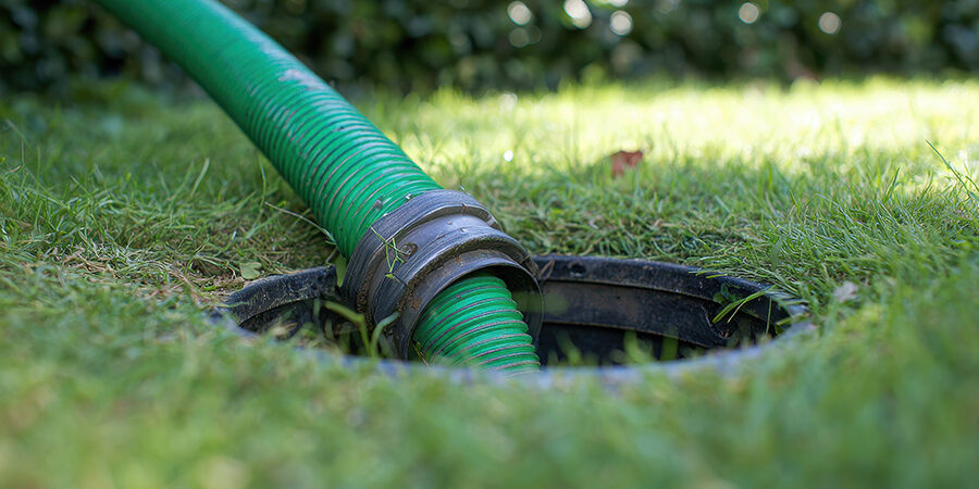 Septic pumping hose inserted into tank opening in a residential yard